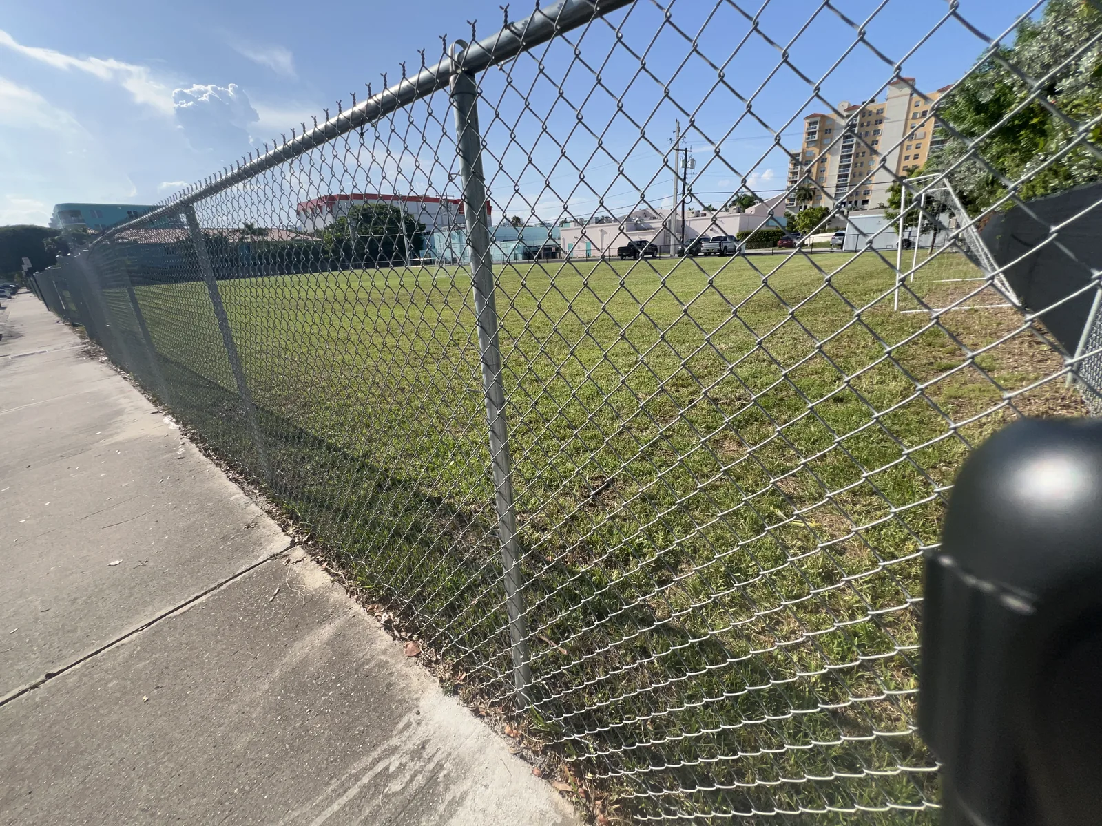 Sidewalk beside the chain-link fence and grass field at Ansin Family Park on Treasure Island