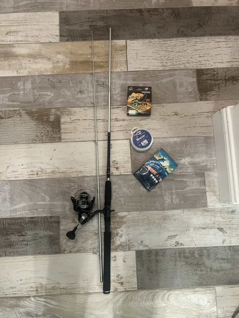One fishing rod in two pieces, a spinning reel, packaged line and tackle laid out on a tile floor