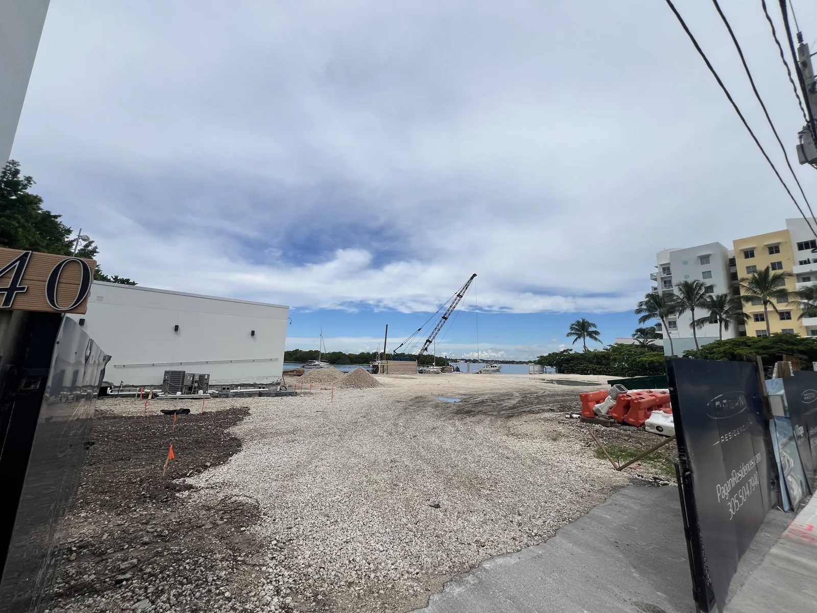 View through the Pagani Residences entrance toward gravel-covered ground, a crane and Biscayne Bay