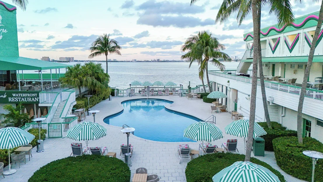 Palm Tree Club’s pool between the hotel wings, with striped umbrellas and Biscayne Bay beyond