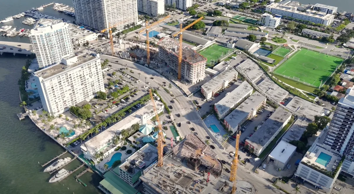 Aerial view of Shoma Bay and Continuum construction sites, with cranes, waterfront buildings and the soccer field beside Shoma Bay at upper right.